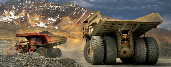 Two mining trucks in a quarry with mountains in the background